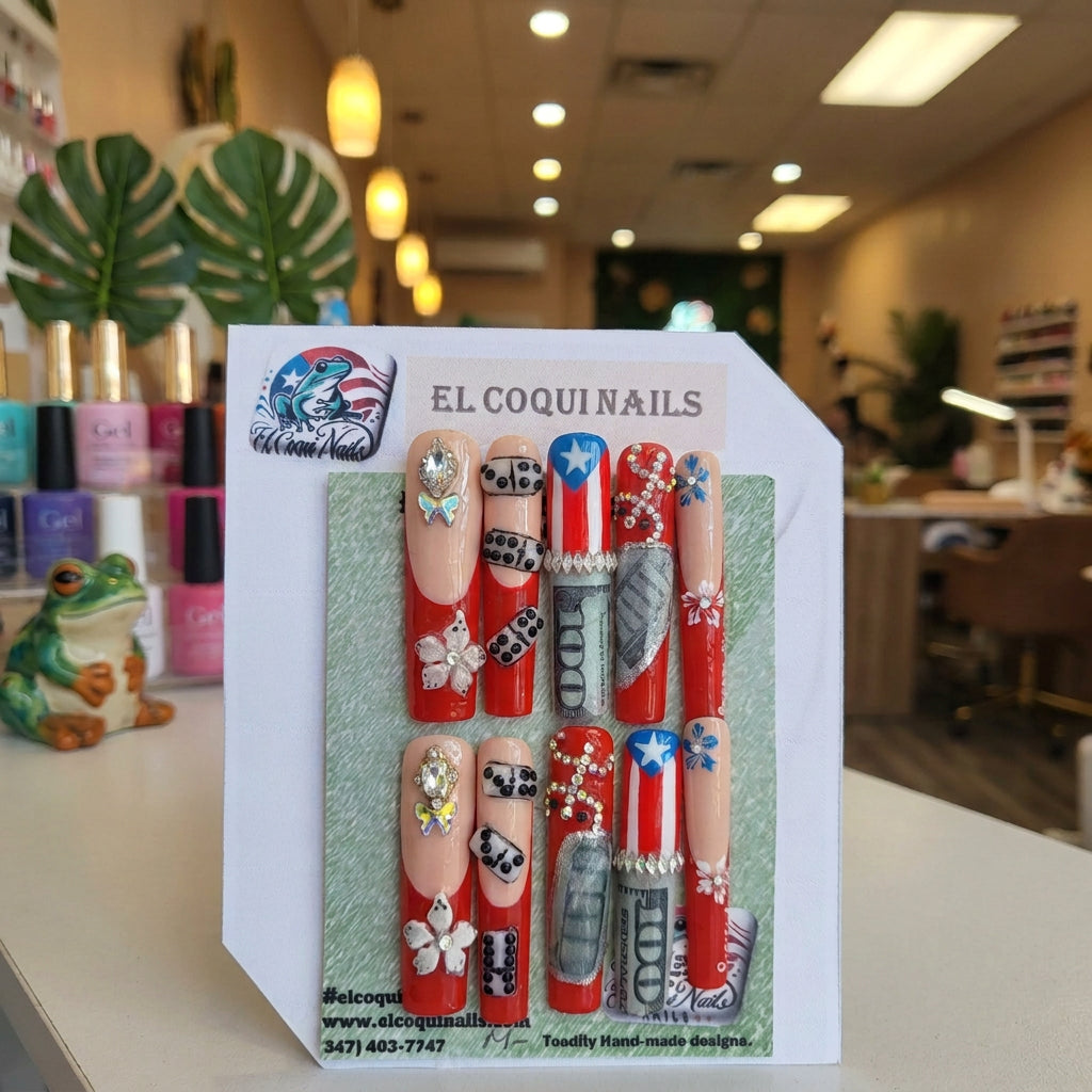 A set of 12 custom press-on nails displayed on a green backing card under the brand name 'EL COQUINAILS'. The nails feature a patriotic American theme with red, white, and blue designs, including stars, stripes, dollar bills, dice, and flowers, embellished with rhinestones.