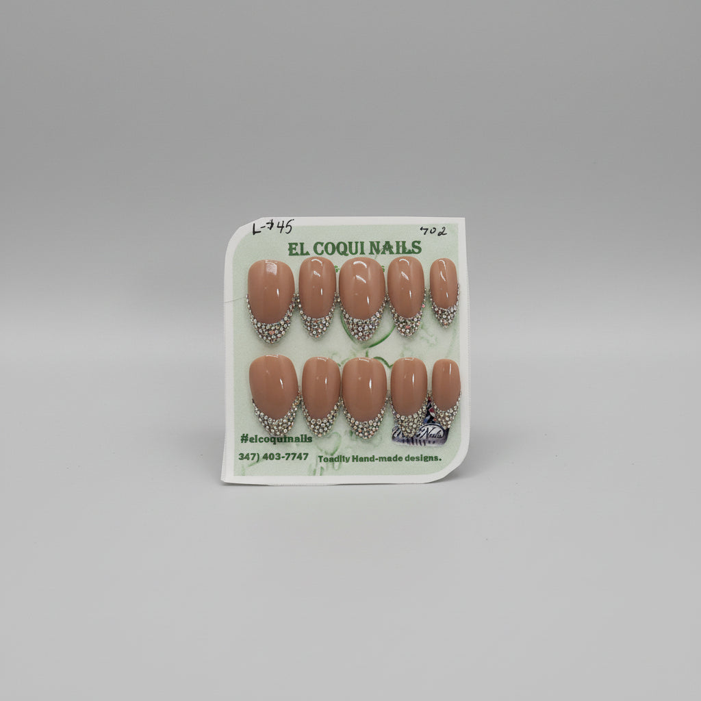 A set of 10 press-on nails on a display card, featuring a glossy nude brown base with a silver rhinestone French tip design. The brand 'EL COQUI NAILS' is printed on the card, and a white label at the bottom displays the style number '702'.