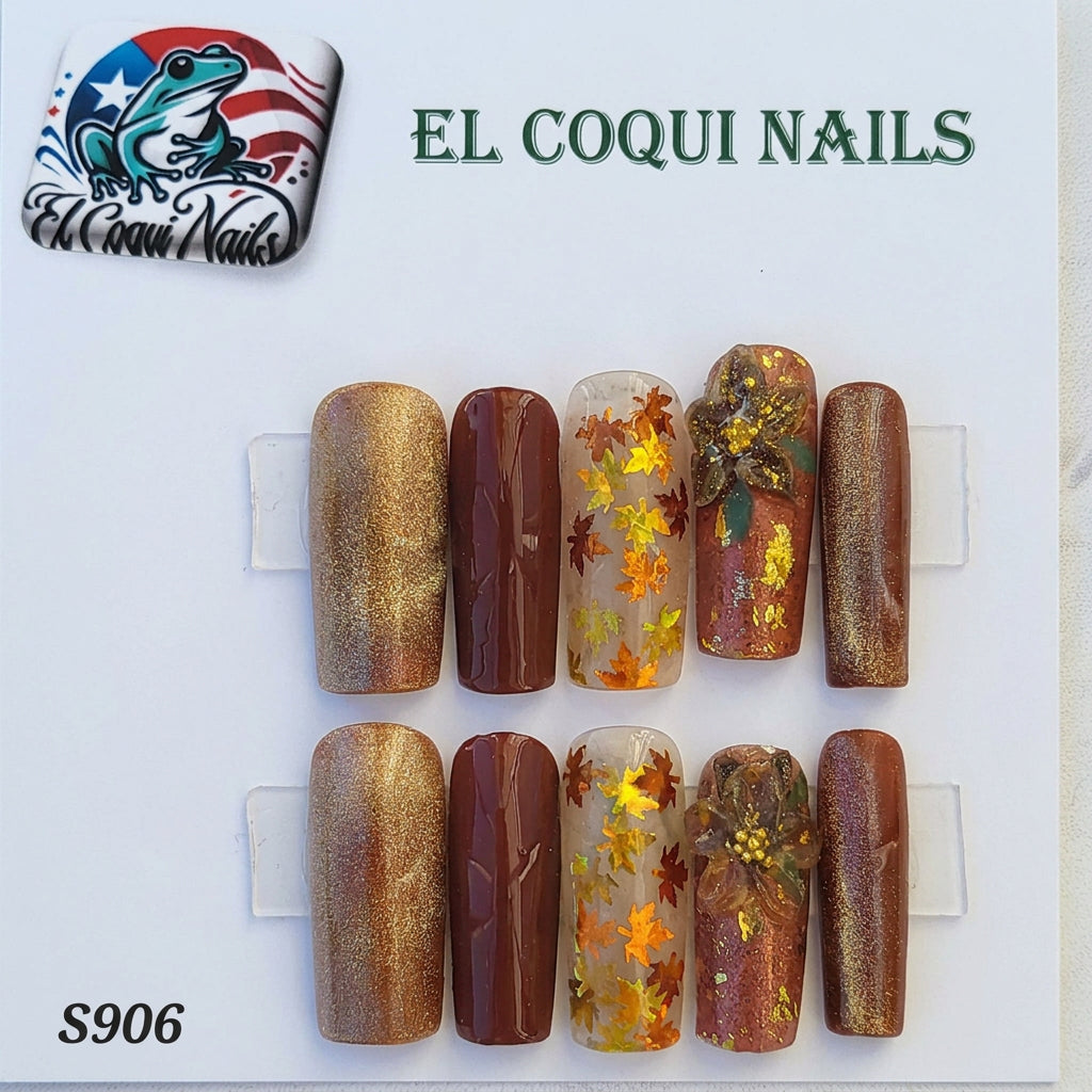 A set of 10 press-on nails displayed on a card, featuring autumn and fall-themed designs. The nails include metallic gold, deep brown, and clear designs with orange and yellow maple leaves and gold foil.