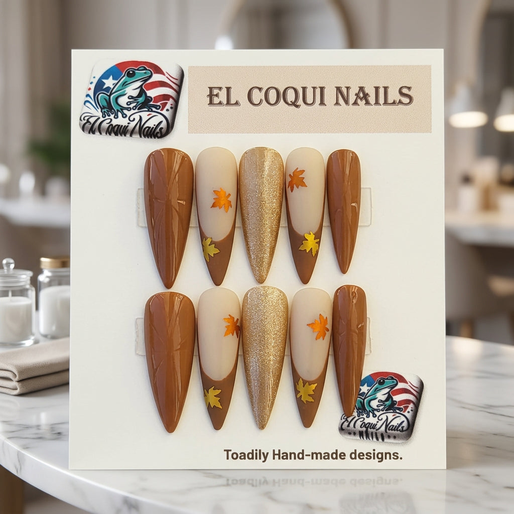 A set of 10 press-on false nails displayed on a branded card. The nails feature a mix of solid medium brown, beige with orange and yellow autumn leaf decals, and a shimmering champagne gold finish.