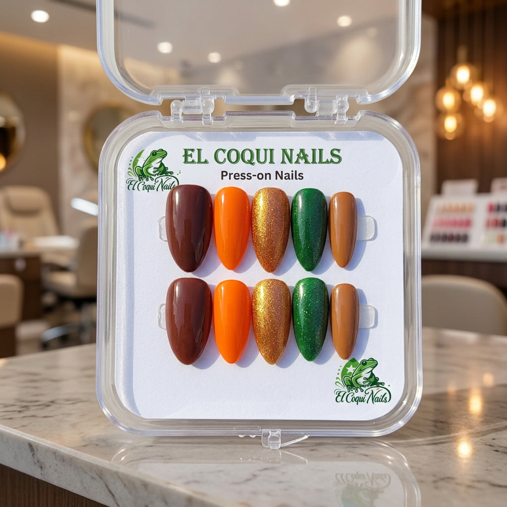 A clear plastic clamshell case of El Coqui Nails press-on nails on a white surface. The nails are arranged in two rows of six and include shades of dark brown, bright orange, metallic gold glitter, emerald green, and tan.