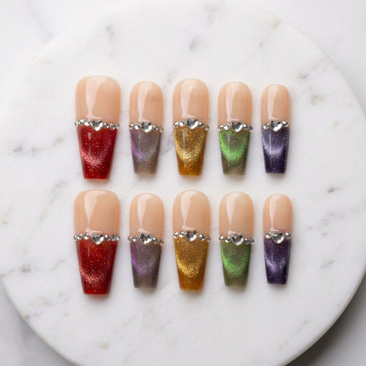 A set of false press-on nails on a backing card labeled EL COQUINAILS, displayed on a white surface. The nails feature a nude beige base with rhinestone trim and come in multiple colors including red, orange, gold, green, purple, and pink.