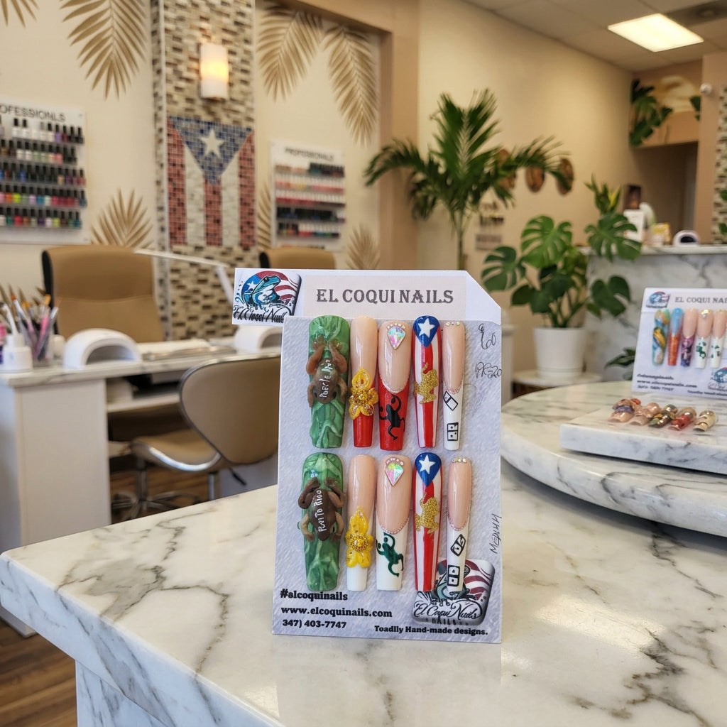 A set of 10 custom decorative press-on nails displayed on a gray card under the brand name 'EL COQUINAILS'. The nails feature patriotic designs including the American flag, camouflage patterns, gold glitter, and rhinestones.