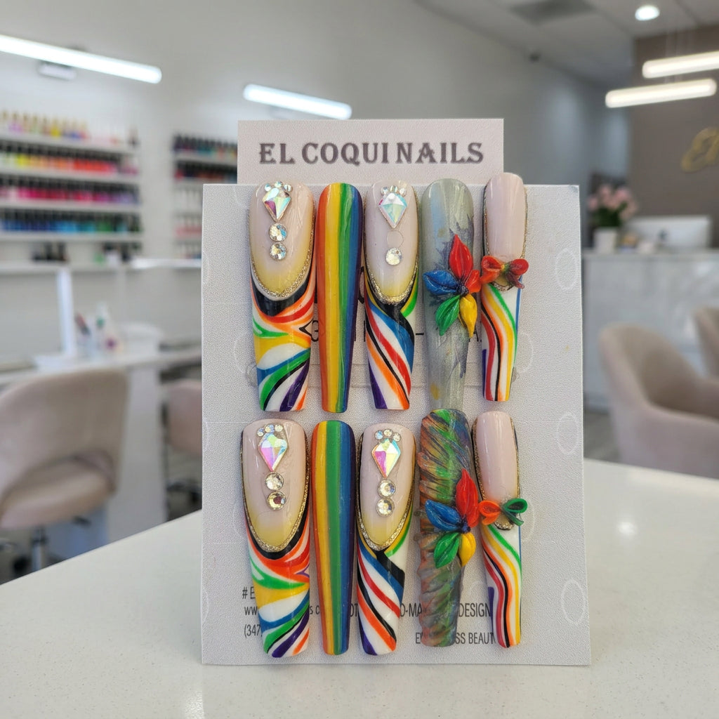 Six decorative press-on nails displayed on a branded card labeled EL COQUINAILS. The nails feature rainbow stripe patterns, rhinestone embellishments, and multicolor floral accents on a light gray background.